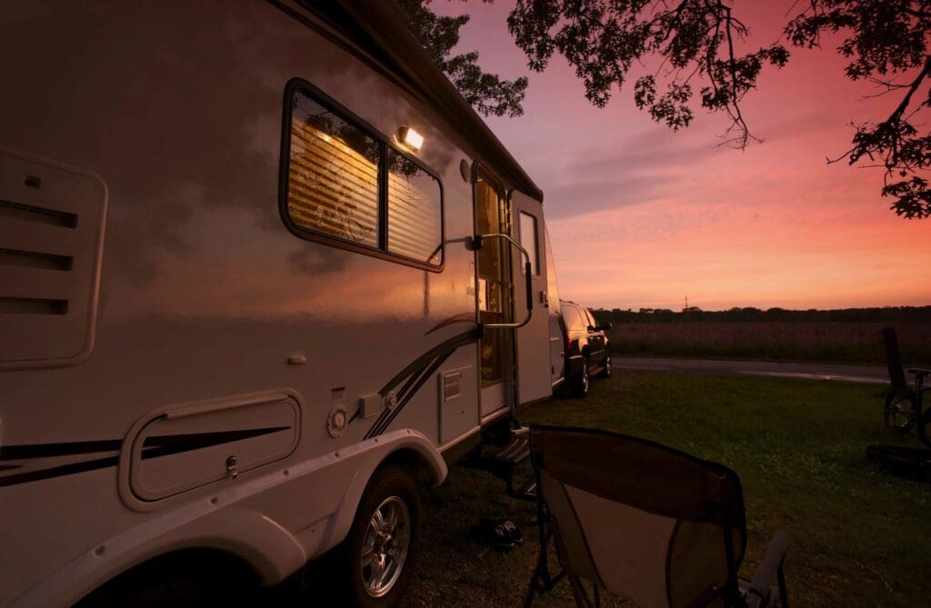 A camper trailer parked at sunset with a chair outside.