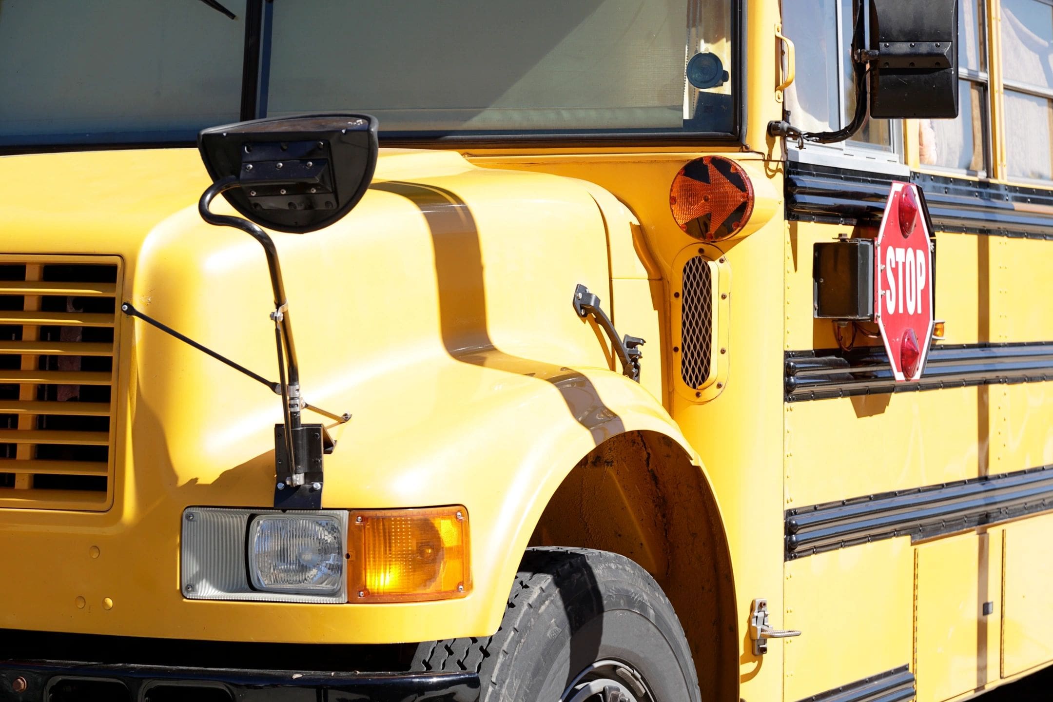 Close-up of a yellow school bus front section showing headlights and mirror.