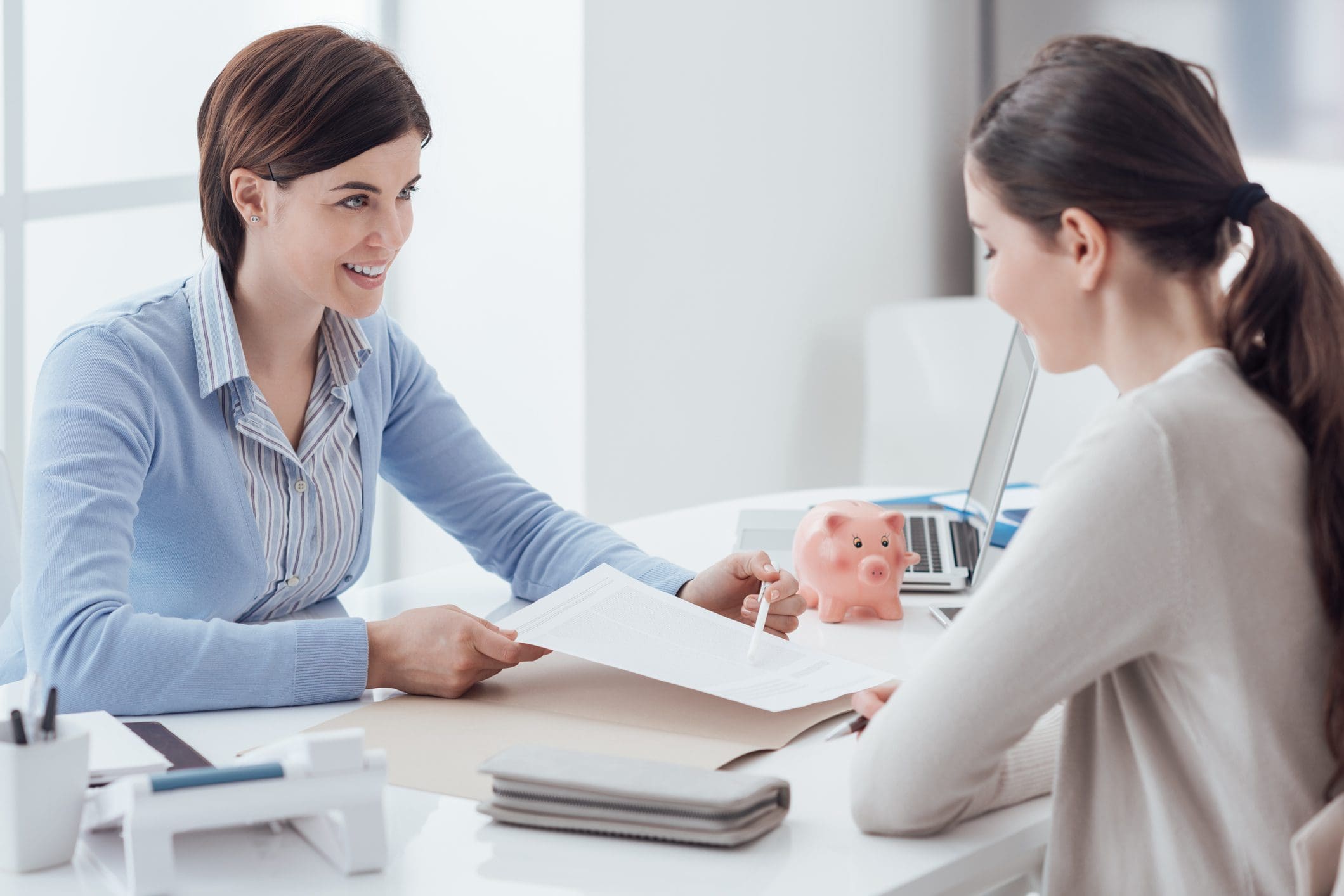 Two women discussing documents at desk.