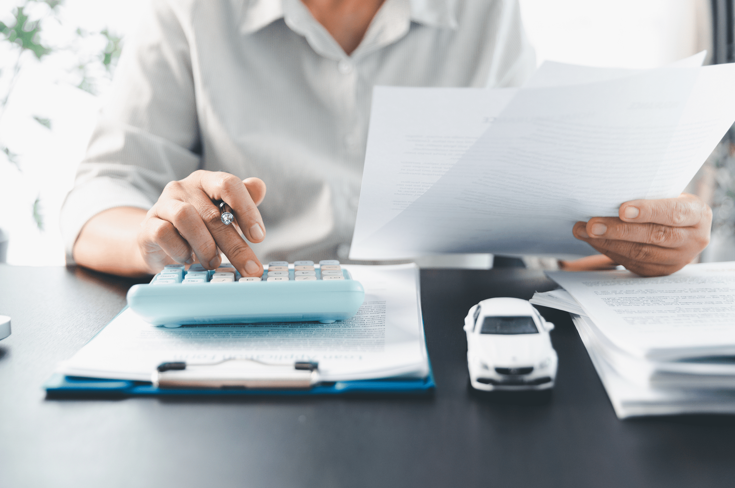Person calculating with papers and toy car.