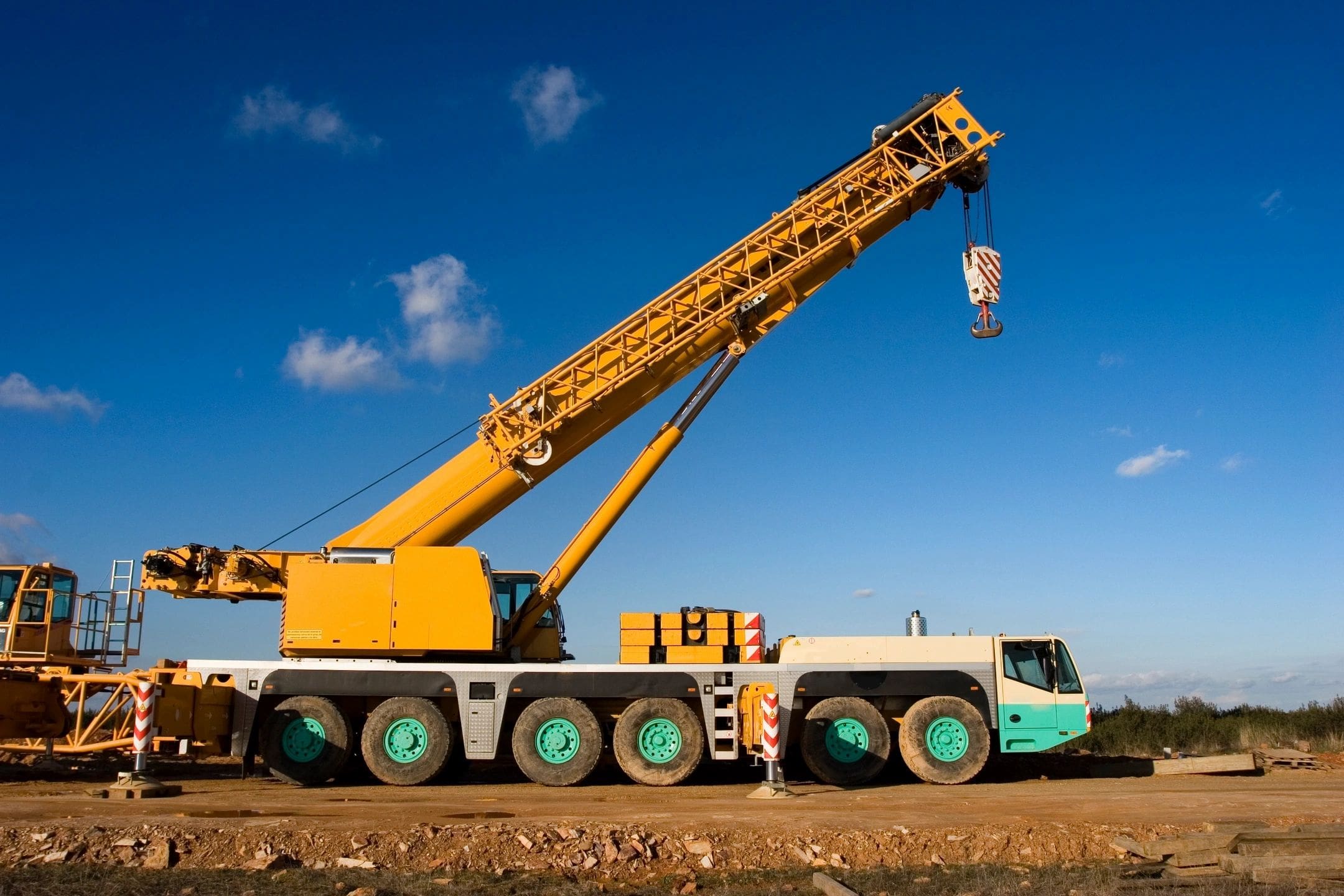 A large yellow crane truck on a construction site under a blue sky.