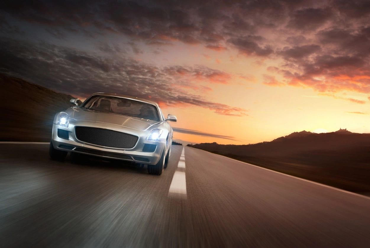 A silver sports car speeding on a highway at sunset.