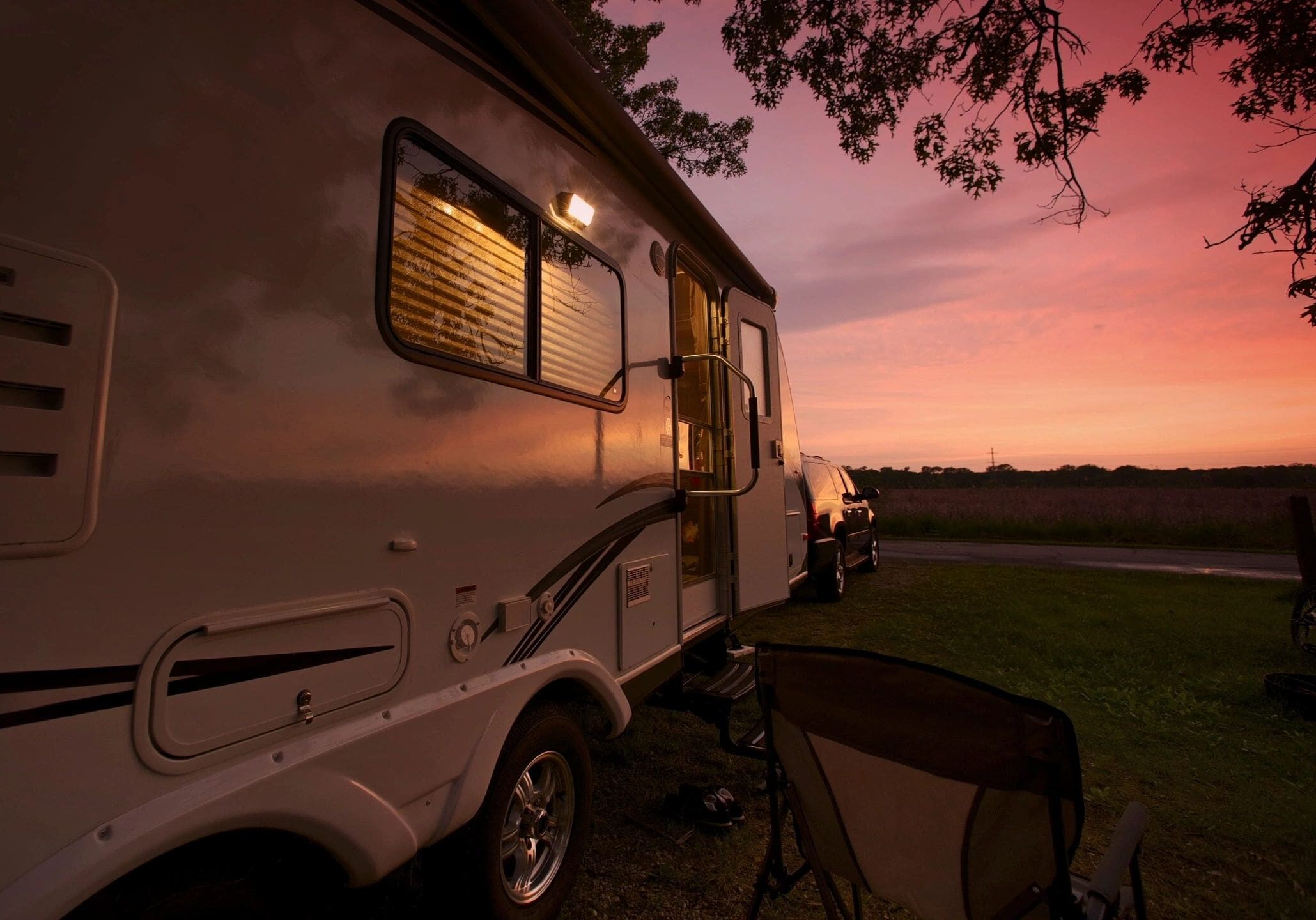A camper trailer parked at sunset with a chair outside.