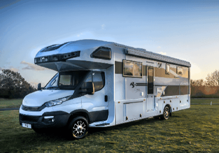 A modern white motorhome parked on grass during sunset.